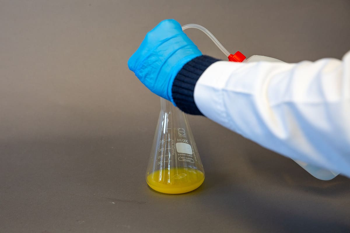 Behandschuhte Hand schwenkt einen Kolben mit gelber Lösung während einer Titration