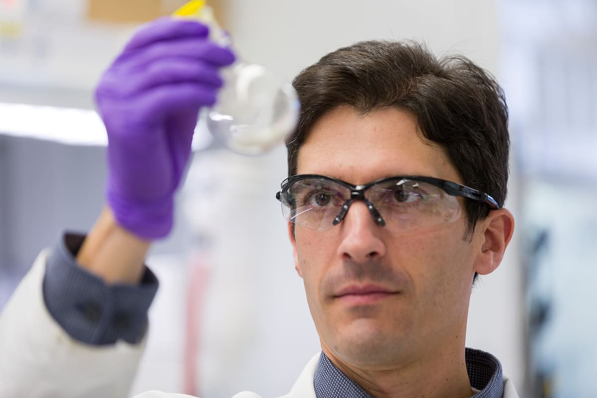 Wissenschaftler mit Schutzbrille hält ein Probengefäß gegen das Licht