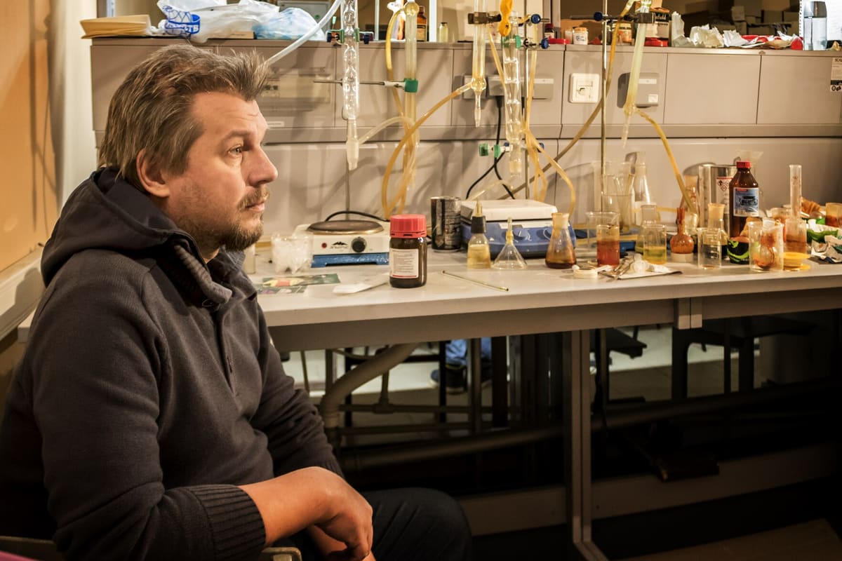Chemiker an einer dicht belegten Laborbank mit Glasapparaturen