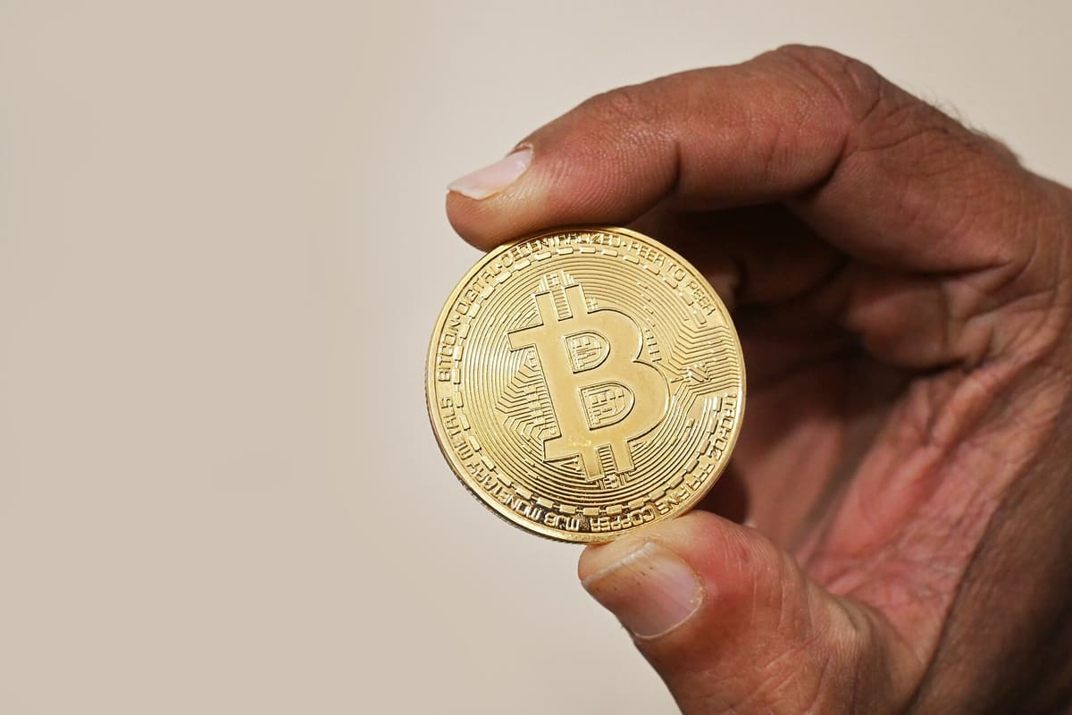 Hand hält eine goldfarbene Bitcoin-Gedenkmünze