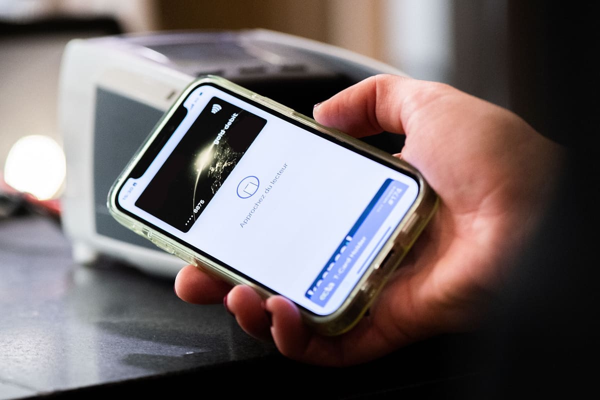Person hält ein Smartphone an ein Bezahlterminal