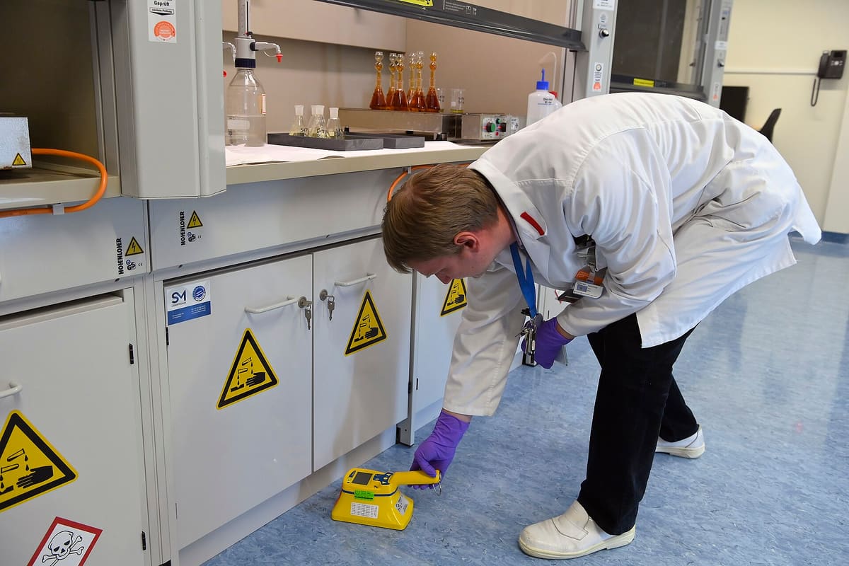 Wissenschaftler kontrolliert ein Gerät an einem Laborschrank mit Warnkennzeichnung