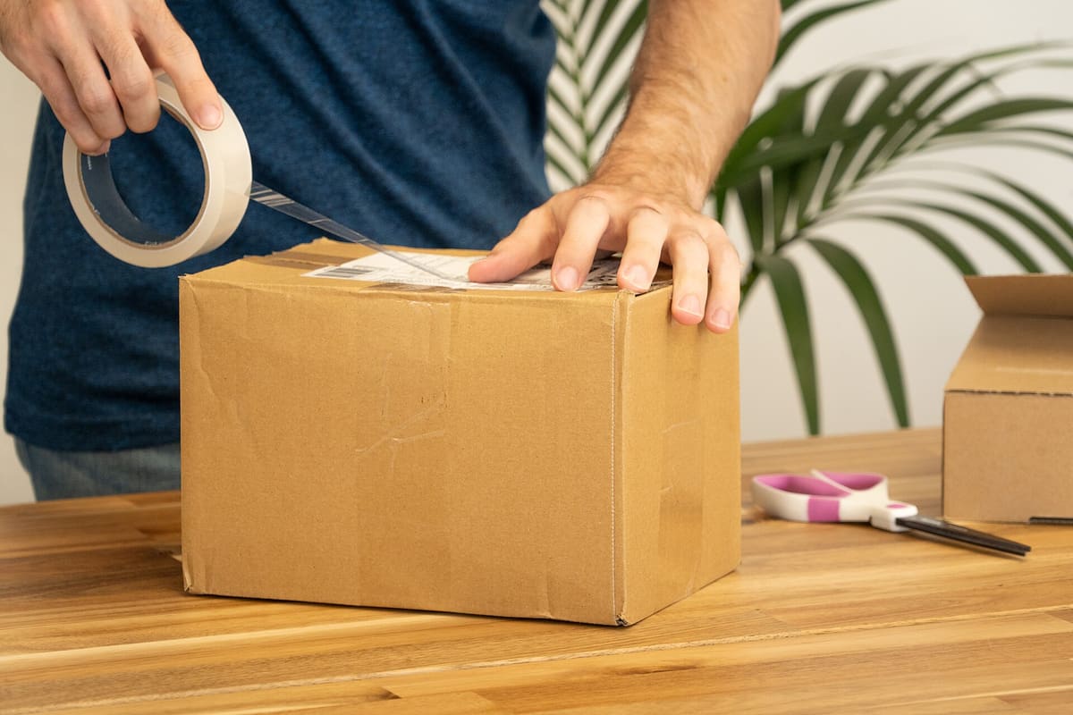 Hände kleben einen Versandaufkleber auf einen Pappkarton